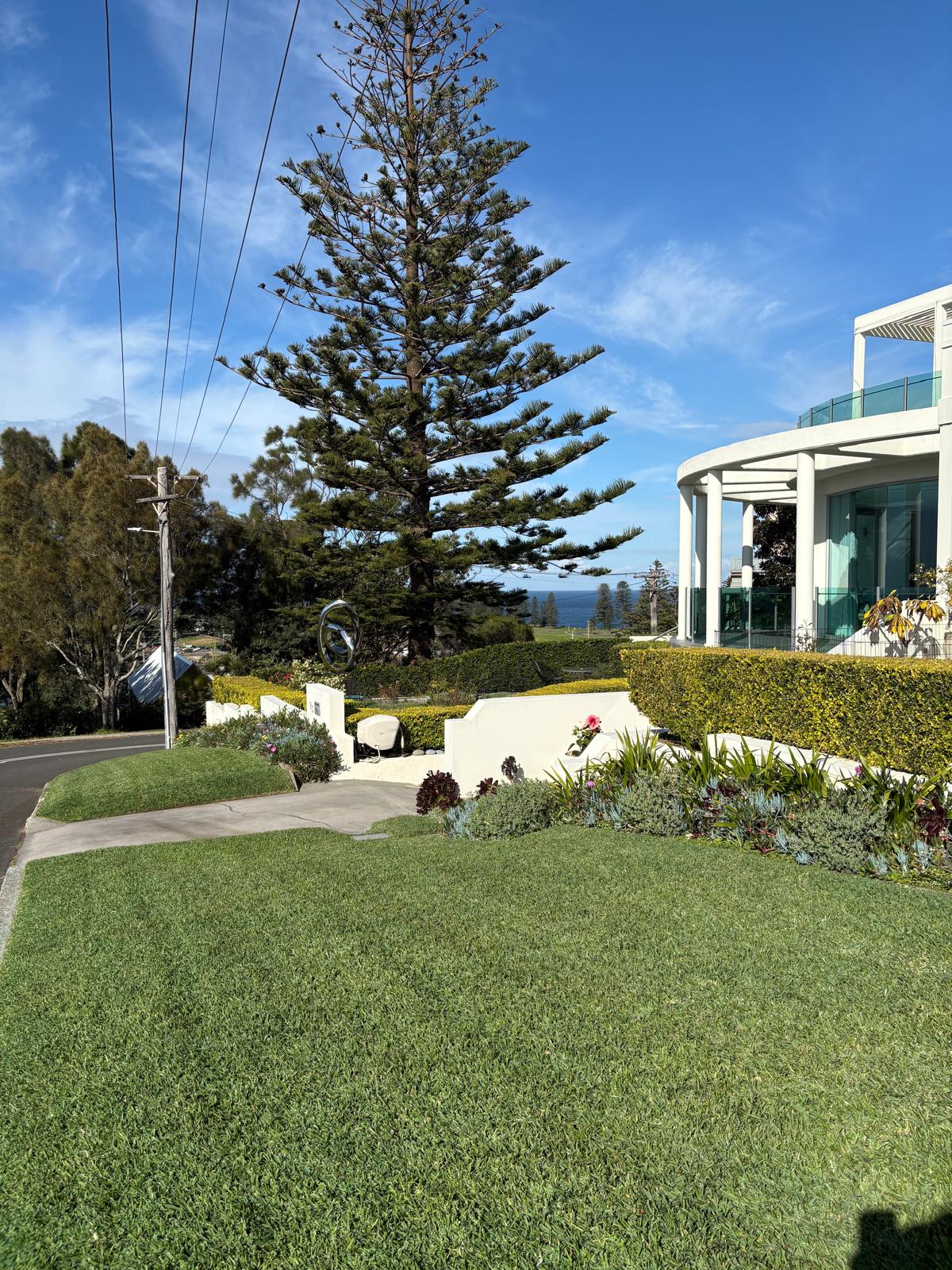 Landscaped coastal home with neatly maintained lawn, garden beds and hedge