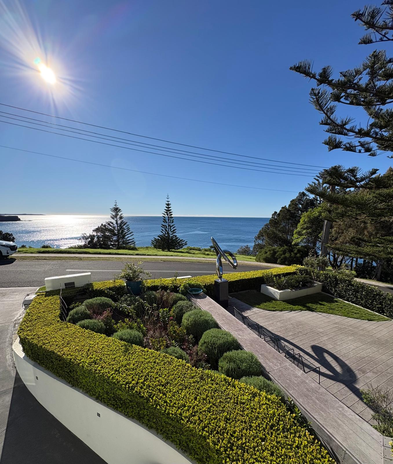 Sculpted coastal garden with clipped hedges, mature trees and ocean view