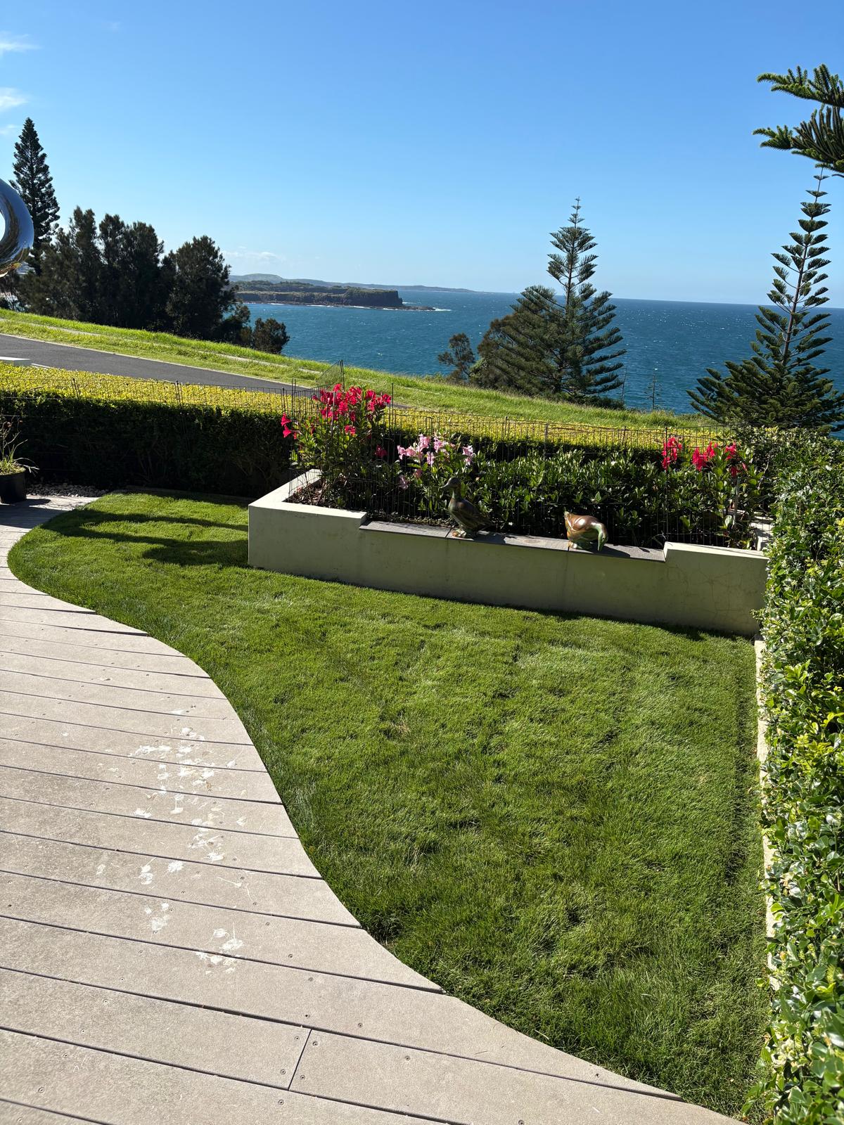 Curved green lawn beside a timber deck overlooking the ocean